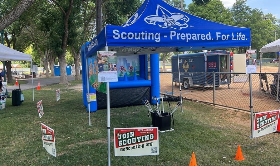 A mobile archery booth with "Join Scouting" yard signs scattered around